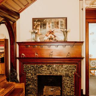 A cozy vintage room with an ornate wooden fireplace and artwork above the mantel.