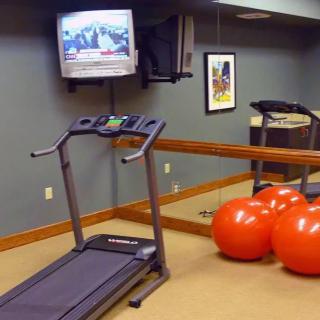 A small gym with a treadmill, exercise balls, and a wall-mounted television.