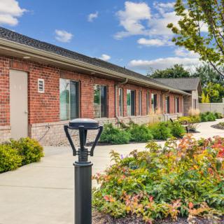 A brick building with a landscaped garden and pathway, featuring outdoor lighting under a partly cloudy sky.