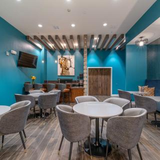 A modern dining area with blue walls and wooden flooring, featuring tables, chairs, and a television.