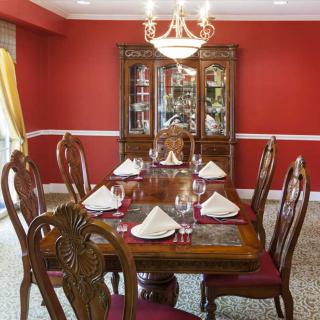 A formal dining room with a wooden table and elegant decor, featuring red walls and a chandelier.
