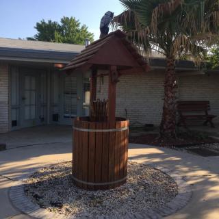 A wooden well in a sunny yard with surrounding garden decor.