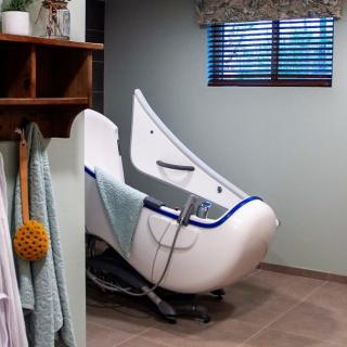 A modern and uniquely shaped bathtub in a well-lit bathroom with towels hanging nearby.