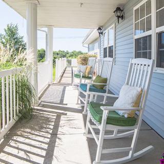 A sunny porch with white rocking chairs and pillows, perfect for relaxation.
