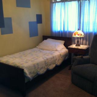 A cozy bedroom with a single bed, side table, and chair.