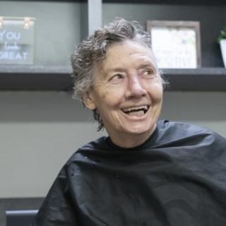 A person smiling while sitting in a hair salon.
