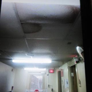 A view of a damaged ceiling in an indoor hallway, showing signs of water damage.