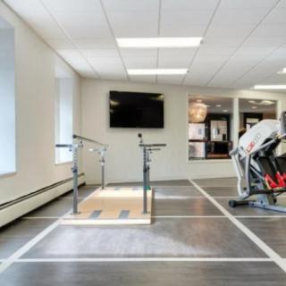 A bright gym interior with exercise equipment, including a treadmill and parallel bars, designed for fitness and rehabilitation.