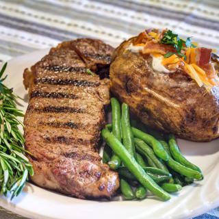 A delicious dinner featuring a grilled steak, a baked potato with toppings, and a side of green beans.