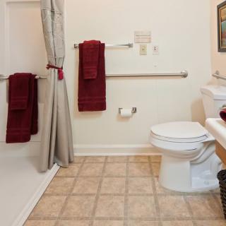 A clean bathroom with a tiled floor, featuring a toilet, shower area, and maroon towels.