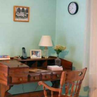 A cozy home office corner with a wooden desk and chair, accented by a lamp and wall clock.