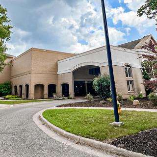 A modern building with a welcoming entrance and landscaped surroundings under a partly cloudy sky.