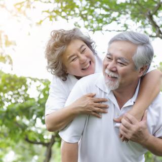 A joyful elderly couple enjoying a playful moment outdoors surrounded by nature.