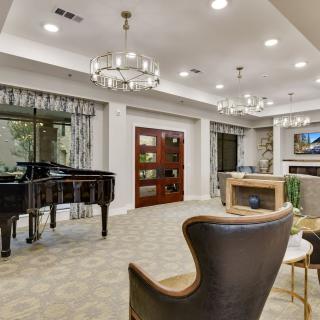 A luxurious living room featuring a grand piano, elegant chandeliers, and a cozy seating area by the fireplace.