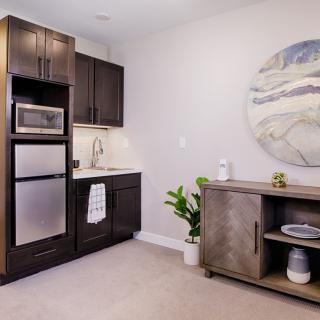 A modern kitchenette with dark cabinets, a microwave, small fridge, and minimalist decor.