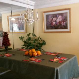 A dining room with a table set with a green tablecloth, adorned with a centerpiece of oranges and greenery. A chandelier hangs above, and the walls feature mirrors and framed artwork.