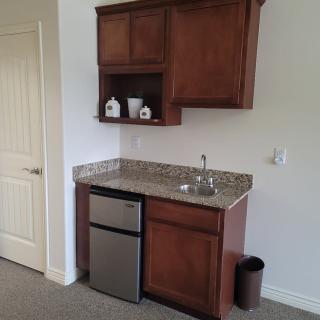 A compact kitchenette with wooden cabinets, a mini fridge, and a granite countertop.