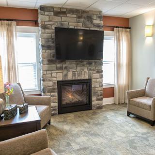 A cozy living room featuring a stone fireplace with a mounted television, surrounded by comfortable armchairs and large windows.