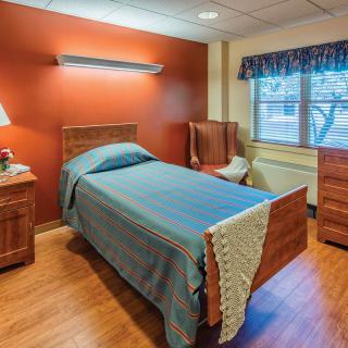 A cozy bedroom with a single bed, wooden furniture, and a window overlooking the outside.