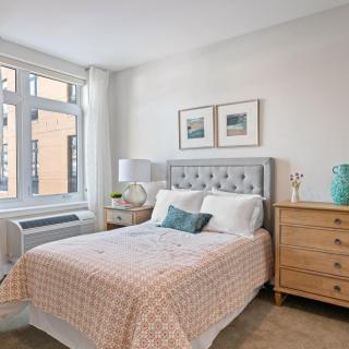 A bright, cozy bedroom with a plush bed, stylish decor, and natural light streaming through a large window.