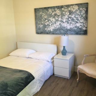 A minimalist bedroom featuring a bed, nightstand, lamp, and artwork on the wall.