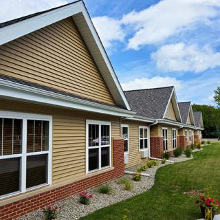 A row of suburban houses with slanted roofs and well-maintained lawns under a partly cloudy sky.