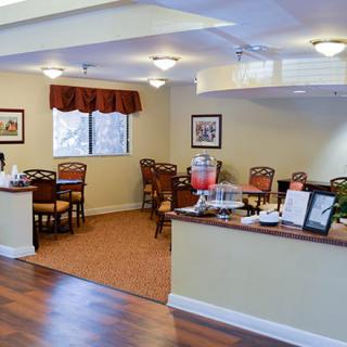 A cozy dining area with wooden chairs and tables, featuring warm lighting and a mix of carpet and wood flooring.