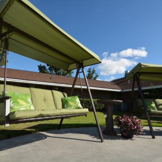 Two outdoor swings with green canopies and cushions on a sunny patio.