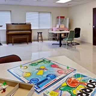 A cozy community room featuring a piano, board games on the table, and seating arrangements for social interaction.