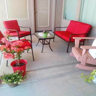 A cozy outdoor porch setup with red chairs, a small table, and colorful flowers.