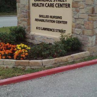 Sign for Lawrence Street Health Care Center with surrounding flowers and landscaping.
