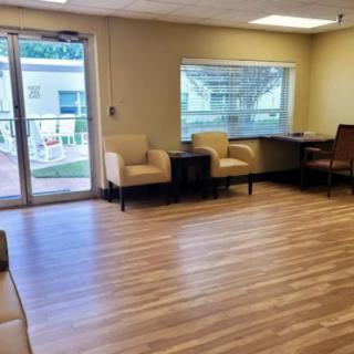 A spacious waiting room with chairs, a table, and large windows providing natural light.