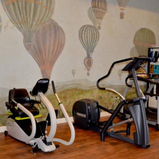 A fitness room features a stationary bike and an elliptical trainer set against a hot air balloon mural on the wall.