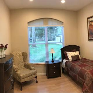 A cozy bedroom featuring a twin bed, an armchair, and a window that brings in natural light.