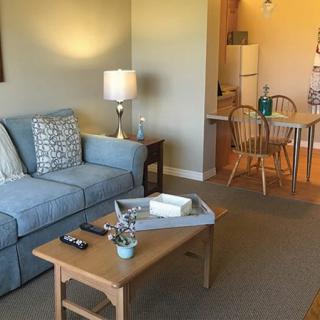 A cozy living room with a blue sofa, wooden coffee table, and a lamp, leading into an open dining area.