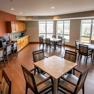A modern dining room with tables and chairs, featuring large windows and a kitchen area.