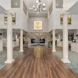 A modern lobby with elegant columns, a central chandelier, and a spacious seating area surrounding a fireplace.