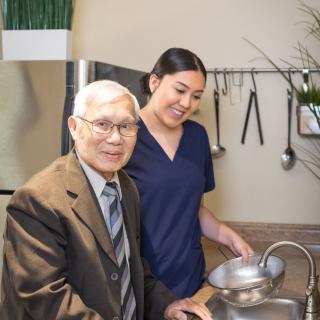 An elderly man and a caregiver in a kitchen setting.