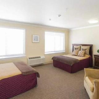 A hotel room with two beds, carpeted floor, and large windows.