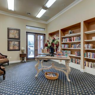 A cozy library room with bookshelves, a central table decorated with flowers, and comfortable seating.