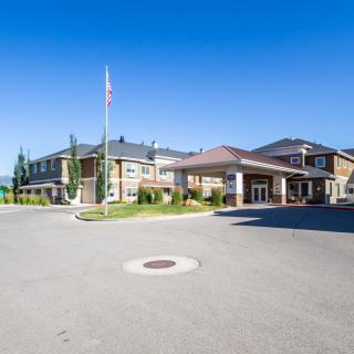 A large building with an entrance and driveway, featuring a flagpole against a clear blue sky.