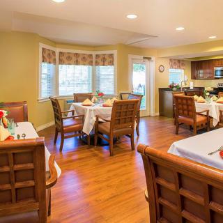 A cozy dining area with neatly arranged tables and chairs, wood flooring, and large windows with curtains.
