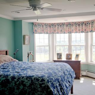 A serene and softly decorated bedroom featuring a cozy bed with blue bedding and large windows that let in natural light.