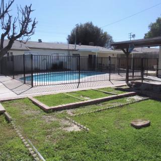 A backyard featuring a fenced swimming pool, green lawn, and patio area.