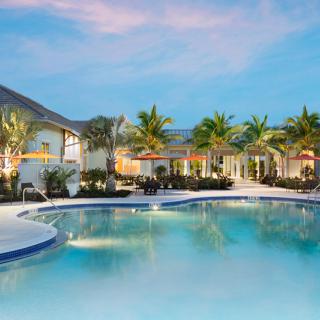 A luxurious resort with a sparkling swimming pool surrounded by palm trees at sunset.