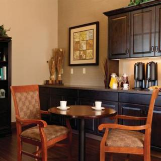 A cozy dining nook with a round table, two wooden chairs, and a coffee station against the wall.