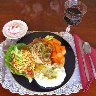 A well-presented dinner plate featuring a main course with salad, carrots, mashed potatoes, and a glass of red wine, accompanied by a dessert.