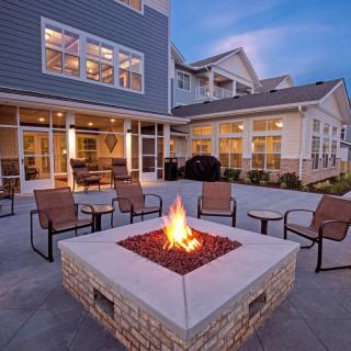 An inviting outdoor patio area with a fire pit surrounded by chairs in front of a building at dusk.