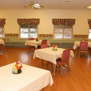 A cozy dining room with tables and chairs, featuring decorative centerpieces and patterned curtains.