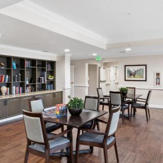 A modern and spacious room with tables, chairs, and a bookshelf, featuring tasteful decor and artwork.